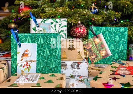 Ein Haufen verpackter Weihnachtsgeschenke liegt unter dem Weihnachtsbaum. Sie sind in verschiedene gemusterte Geschenkpapiere eingewickelt und mit Geschenkanhängern versehen. Stockfoto