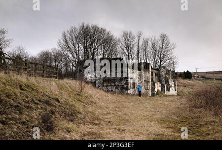 Eine Frau schaut in das Fenster der ehemaligen Horse and Jockey Pub Ruin im Troak Hey NOOK, Castleshaw bei Standedge, Saddleworth Stockfoto