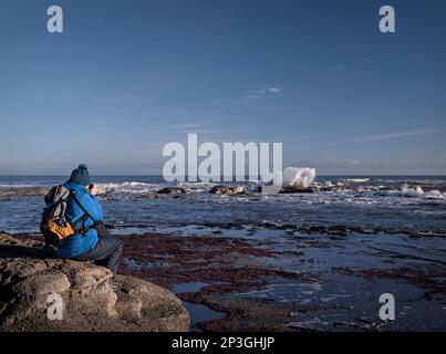 Eine Fotografin fotografiert Wellen in der Saltwick Bay bei Whitby, North Yorkshire Stockfoto