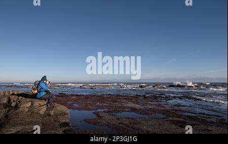 Eine Fotografin fotografiert Wellen in der Saltwick Bay bei Whitby, North Yorkshire Stockfoto