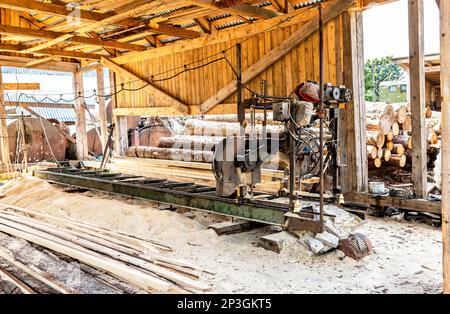 Altes Holzsägewerk für die Bearbeitung von Stämmen in Maschinen Sägewerk Säge sägt den Baumstamm auf den Planken. Holzsägemehl, Werksägen von Holz, Stockfoto