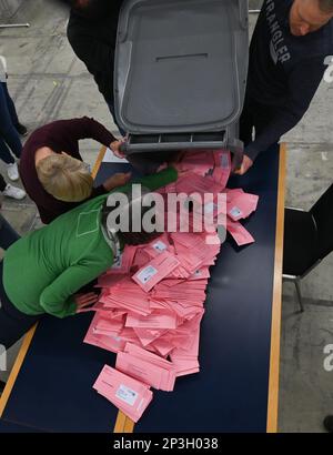 05. März 2023, Hessen, Frankfurt/Main: Wahlhelfer geben an einem Tisch in einer Ausstellungshalle mit abwesenden Wahlzetteln für die Bürgermeisterwahl einen Tipp aus. Etwa 509.000 Einwohner Frankfurts werden aufgefordert, für einen neuen Stadtführer zu stimmen. Foto: Arne Dedert/dpa Stockfoto