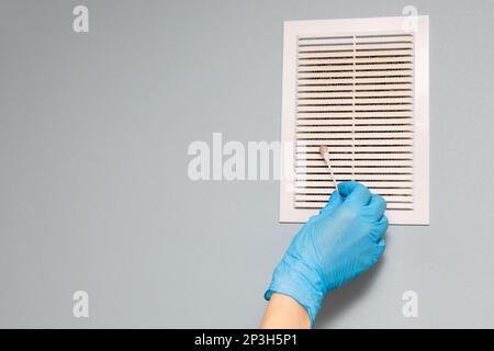 Man prüft den Zustand des Lüftungsgitters. Ein Mann, der den Lüftungsgitter im Zimmer reinigt. Wattestäbchen mit Handgriff. Stockfoto