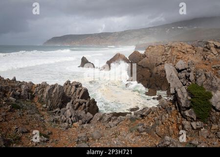 Stürmische Wellen des Atlantischen Ozeans, die auf Felsen unter Forte do Guincho stürzen und nach Norden auf die Landzunge Ponta do Rebolo blicken Stockfoto