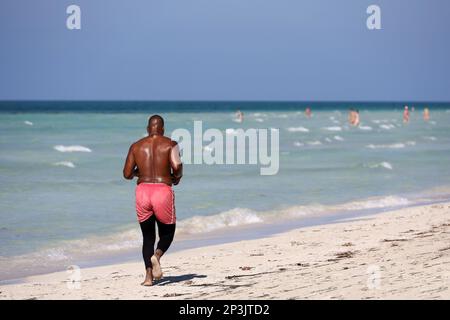 Barfuß-Schwarzer, der im Hintergrund am Sand vorbeiläuft. Workout am Strand, gesunder Lebensstil Stockfoto