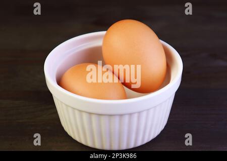 Nahaufnahme von Hühnereiern in einer weißen Schüssel isoliert auf einem schwarzen Holztisch Stockfoto