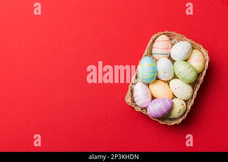 Farbenfrohe Ostereier in Korb mit buntem Hintergrund, Nahaufnahme. Draufsicht mit Kopierbereich. Stockfoto