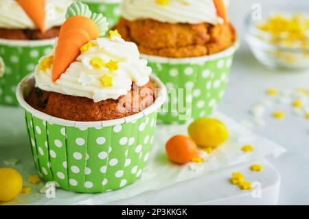 Karottenkuchen Cupcakes zu Ostern. Karotten-Cupcakes mit Frischkäse-Zuckerguss, dekoriert mit winzigen Marzipan-Karotten auf weißem Hintergrund. Frohe Ostern und Stockfoto