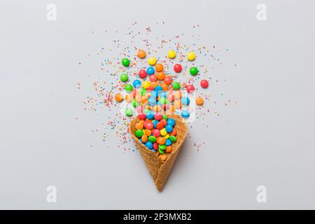 Waffelkonus voller traditioneller Süßigkeiten, die auf farbigen Hintergrund fallen, mit Platz für Kopien. Frohes Weihnachtsangebot. Stockfoto