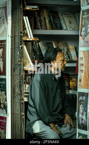 Kalkutta, Indien - 12. Februar 2023: Ein gealterter Buchhändler sitzt inmitten von Bücherregalen und schaut mit Bedacht zur Seite. Selektiver Fokus. Stockfoto