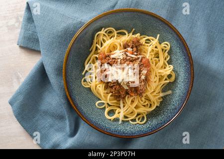 Spaghetti mit Bolognese-Sauce aus Hackfleisch und Tomaten, garniert mit Parmesan auf einem blauen Teller und Serviette, italienisches Nudelgericht, hoher Winkel Stockfoto