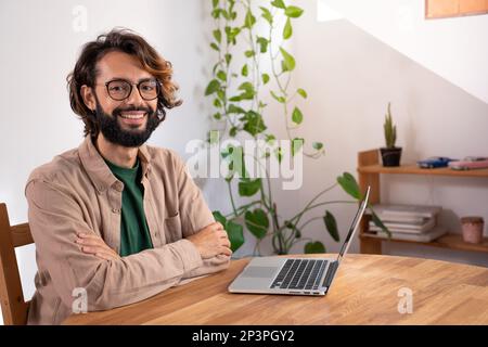 Fröhlicher Mann, der in einem kleinen Unternehmen in der Zentrale in die Kamera schaut. Porträt eines Freiberuflers. Stockfoto