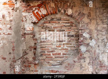 Wandtextur mit altem Putz und abblätterndem Hintergrund mit freiliegendem rotem Ziegel. Alte Backsteinmauern Bogenfenster Stockfoto