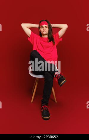 Der Mann warf seine Hände hinter den Kopf und sitzt entspannt auf dem Stuhl im roten Studio Stockfoto