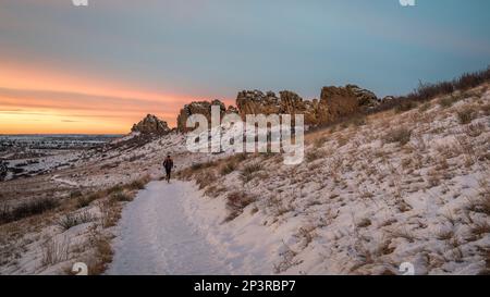 Wintersonnenaufgang über einem Pfad in den Ausläufern von Colorado mit einem Läufer in der Ferne: Devils Backbone Felsformation bei Loveland Stockfoto