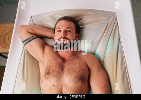 Porträt eines gutaussehenden jungen Mannes mit Bart, der sich auf einem elektrischen Massagebett entspannt und eine Spa-Behandlung im luxuriösen Spa-Salon genießt. Stockfoto