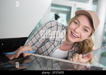 Glückliche Frau, die einen Drucker repariert, während sie die Kamera anlächelt Stockfoto