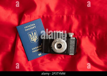 Ausländischer ukrainischer Pass und eine alte Kamera auf rotem Hintergrund, Urlaub Stockfoto