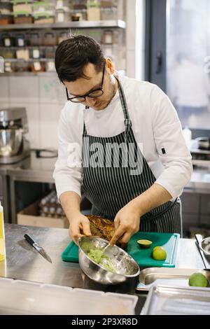 Der Koch bereitet Essen zu. Nahaufnahme eines männlichen Kochs, der Avocado-Toast in einer geräumigen, modernen Küche zubereitet. Stockfoto