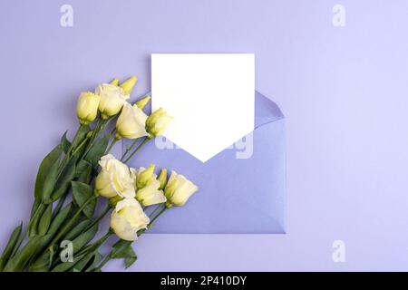Umschlag mit leerer Karte und weißen Eustoma-Blumen auf lila Hintergrund. Valentinstag, Muttertag, Frauentag Konzept. Draufsicht, flach liegend, Modell. Stockfoto