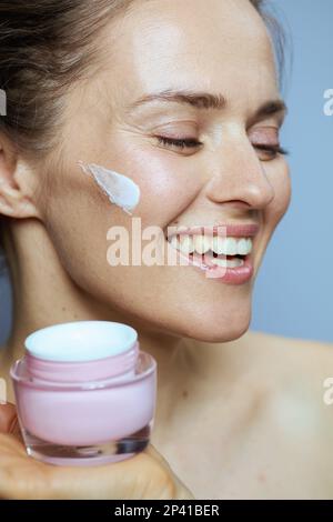 Lächelnde 40-jährige Frau mit kosmetischer Creme auf blauem Hintergrund. Stockfoto