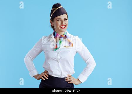 Glückliche, stilvolle Flugbegleiterin vor blauem Hintergrund in Uniform. Stockfoto