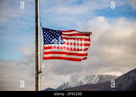 Die Flagge der Vereinigten Staaten von Amerika fliegt im Herbst mit Halbmast und blauem Himmel, Wolken und Berghintergrund im Norden. Stockfoto