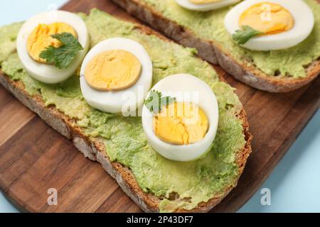 Gehen Sie an Bord mit köstlichen Avocado-Toasts, gekochten Eiern, Petersilie und Tomaten auf blauem Hintergrund Stockfoto