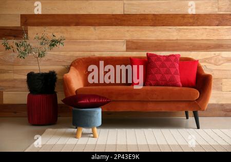 Stilvolle dekorative Kissen auf gemütlichem braunem Sofa in der Nähe der Holzwand Stockfoto