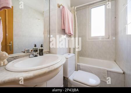 Kleines Badezimmer mit einem quadratischen weißen Porzellanwaschbecken auf einem Holzschrank, einem rahmenlosen Spiegel an der Wand und einer Duschkabine mit Glaskabine Stockfoto