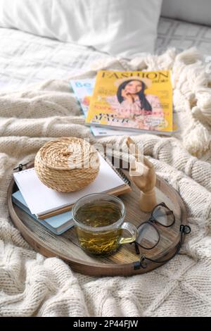 Stilvolles Tablett mit verschiedenen Innenelementen und Tee auf dem Bett Stockfoto