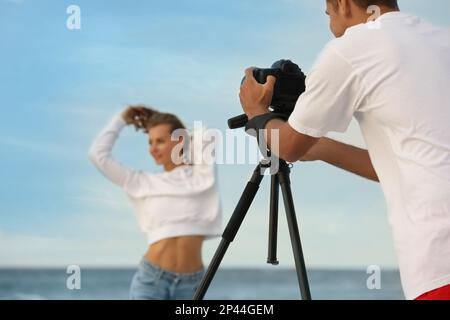 Fotograf fotografiert Modell mit professioneller Kamera in der Nähe des Meeres Stockfoto