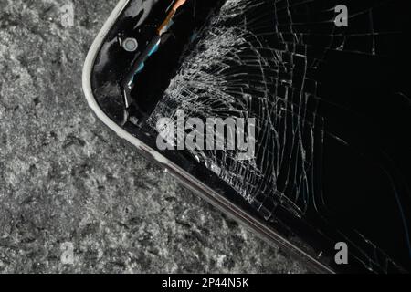 Smartphone mit rissigem Bildschirm auf grauem Steinhintergrund, Nahaufnahme. Gerätereparatur Stockfoto
