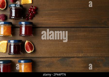 Gläser mit verschiedenen Marmeladen und frischen Zutaten auf Holztisch, flach liegend. Platz für Text Stockfoto