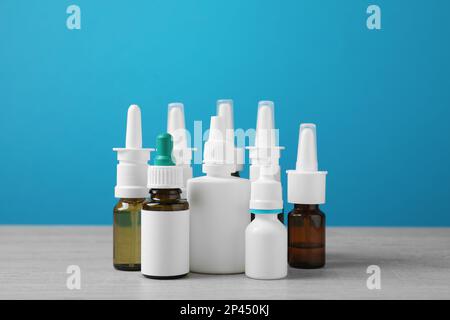 Nasensprays in verschiedenen Flaschen auf weißem Holztisch vor hellblauem Hintergrund Stockfoto