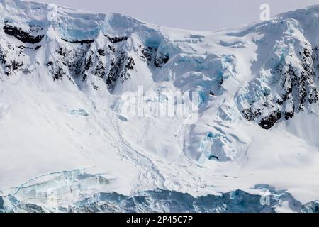 Schneebedeckter Bergkamm, antarktische Halbinsel. Felsen auf schneebedeckten Hängen. Blaues Eis sichtbar. Stockfoto