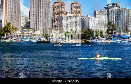 Honolulu, Oahu, Hawaii, USA, - 6. Februar, 2023: Menschen auf Surfbrettern, die von einem kleinen Motorboot und einem Mann in einem Kajak im Hafen von Ilikai gezogen werden Stockfoto