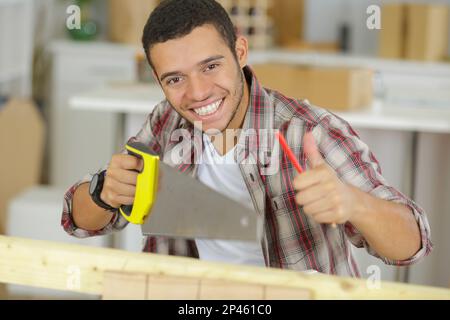 Bauarbeiter, der eine Säge in der Hand hält und mit Daumen nach oben genehmigt Stockfoto