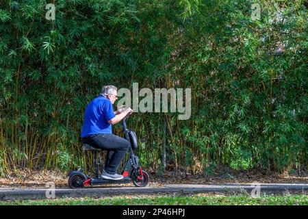 NEW ORLEANS, LA, USA - 1. MÄRZ 2023: Älterer Mann fährt auf seinem Motorroller neben dem Audubon Park auf dem Bürgersteig Stockfoto