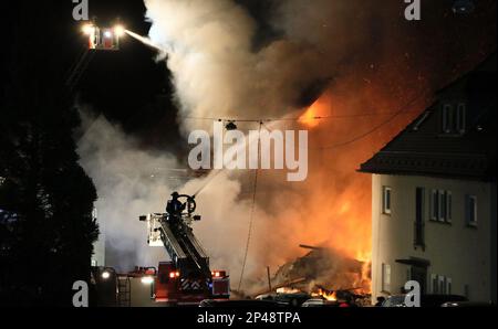 Stuttgart, Deutschland. 06. März 2023. Feuerwehrleute auf Luftleitern löschen ein Wohngebäude. Ein Bewohner wird nach einer vermuteten Gasexplosion in einem Wohngebäude im Westen Stuttgarts vermisst. Ein Teil des Hauses brach in der Nacht bis Montag zusammen, der andere stand laut Feuerwehr in Flammen. Kredit: Andreas Rometsch/KS-Images/dpa/Alamy Live News Stockfoto