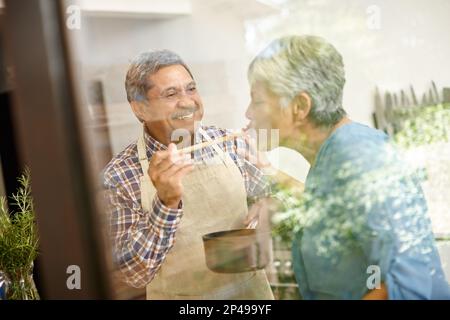Kochen ist Liebe, die essbar ist. Ein glückliches Seniorenpaar, das zu Hause ein gesundes Essen kocht. Stockfoto