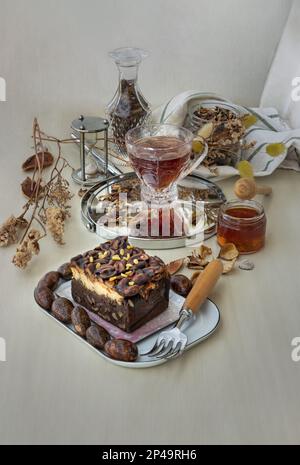 Ein Stück hausgemachter Toffee-Kuchen mit Käsekuchen ist mit geschnittenen Cashew-Nüssen und dunkler Schokolade mit Mandeln und Schmetterlingsblume verziert Stockfoto