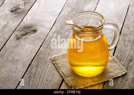 Speiseöl in Glaskanne auf Holztisch Stockfoto