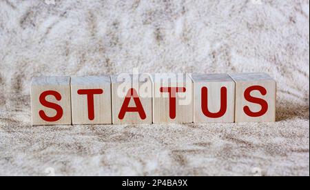 Das Wort STATUS. Holzwürfel mit Buchstaben auf Sandhintergrund. Stockfoto