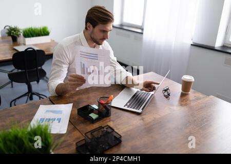 Ein Geschäftsmann, der die Finanzangelegenheiten seiner Firma studiert und Diagramme in der Hand hält Stockfoto