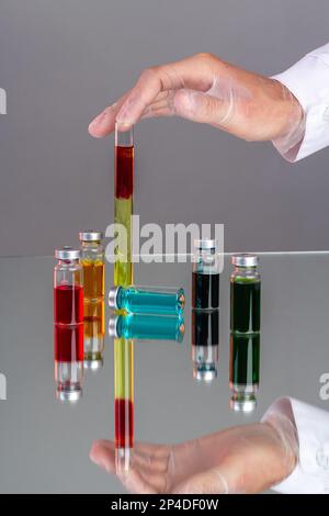 Hand mit Handschuh, die das Reagenzglas mit Blut hält. Arzneimittelfläschchen mit farbiger Lösung. Bunte Impfstoffflaschen. Stockfoto