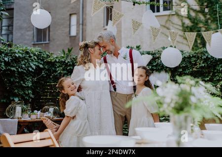 Reife Braut und Bräutigam posieren mit ihren Töchtern bei der Hochzeitsfeier draußen im Hinterhof. Stockfoto