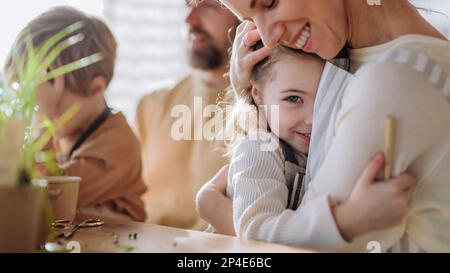 Glückliche Familie pflanzt im Frühling zusammen Kräuter, Mutter umarmt ihre kleine Tochter. Stockfoto