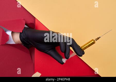Nahaufnahme der handgehaltenen Spritze mit gelbem Glitzer. Roter und gelber Papierhintergrund. Stockfoto
