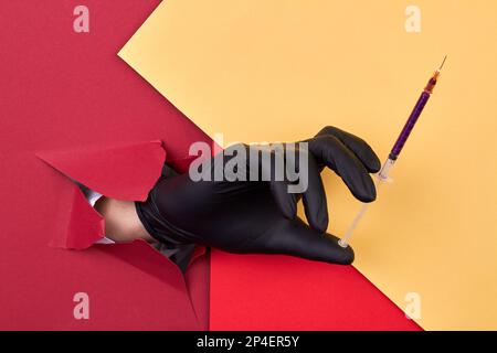 Hand mit schwarzem Handschuh mit Kosmetikspritze und violettem Glitzer. Roter und gelber Papierhintergrund. Stockfoto